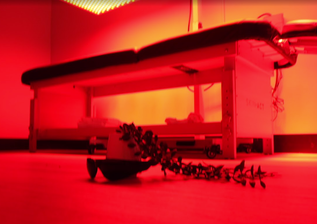 Red-lit scene of a small train or machine on a surface, with tiny figures scattered underneath.