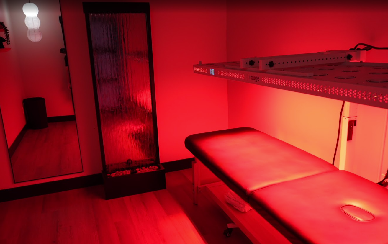 Red-lit massage room with a treatment table, mirror, and shelving unit