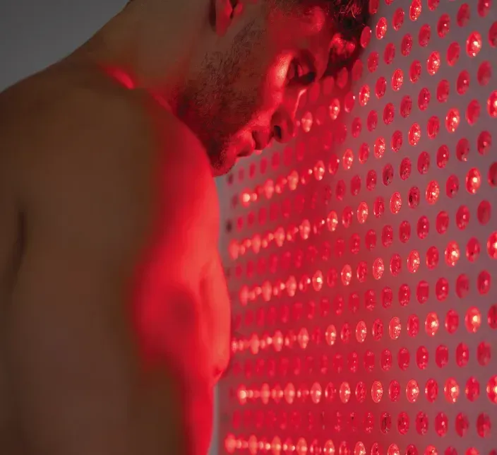 A shirtless man presses his face against a glowing red LED panel.