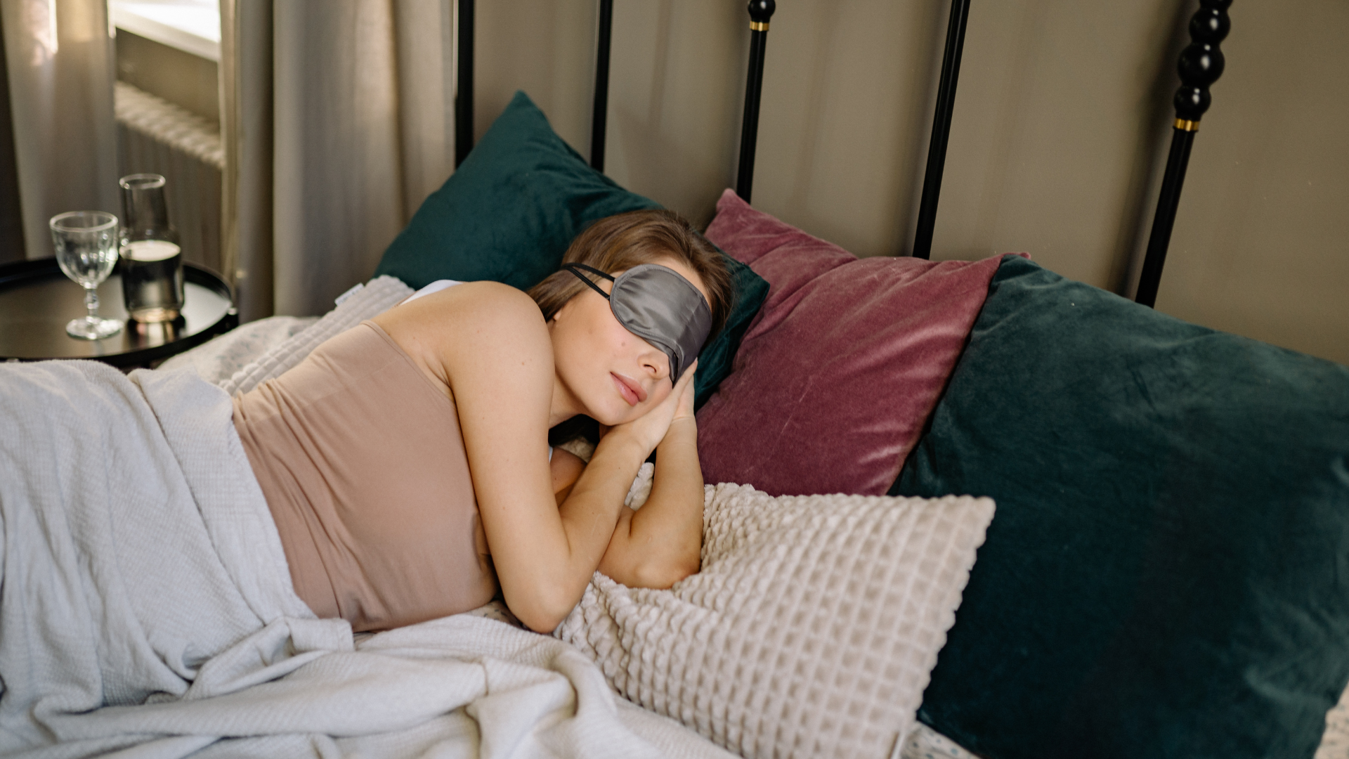 Person sleeping on a bed with pillows and a gray blanket in a softly lit bedroom