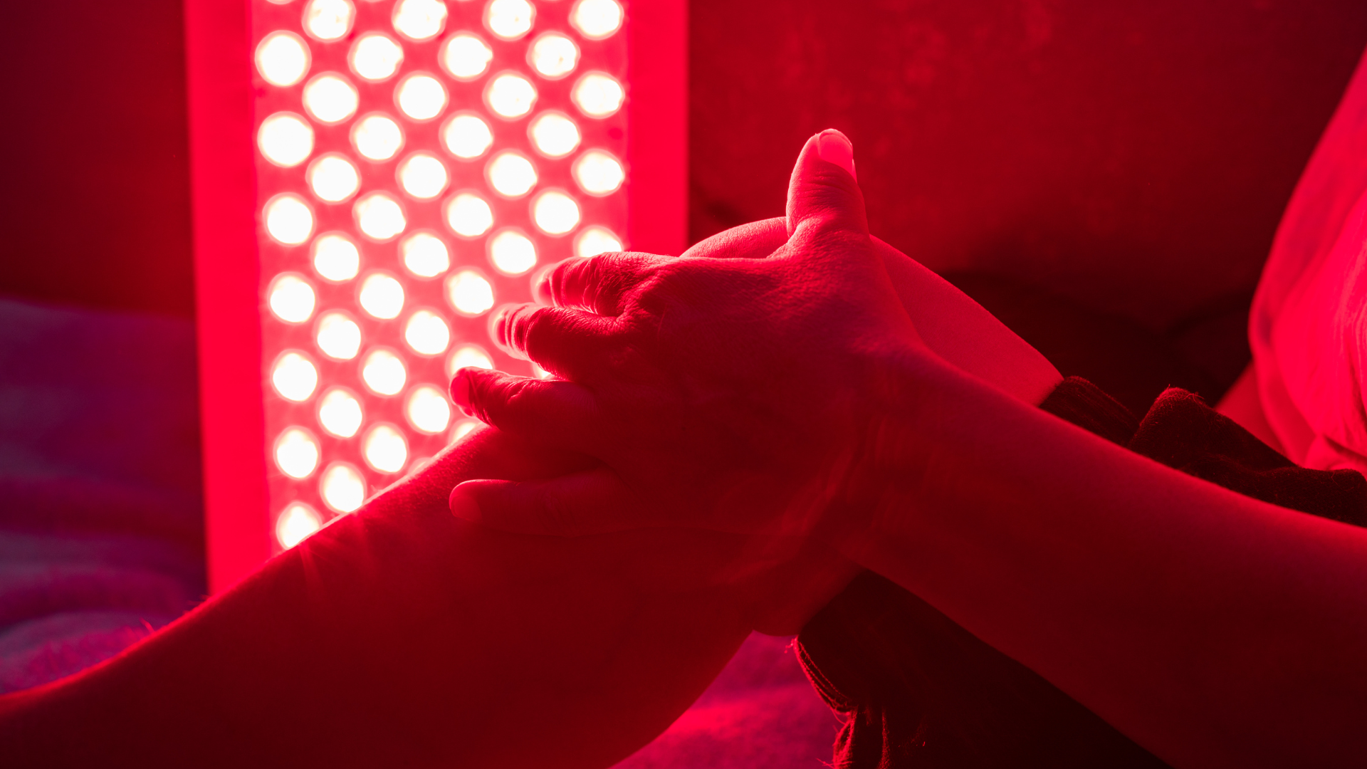 Hands clasped together in red light beside a bright LED panel.