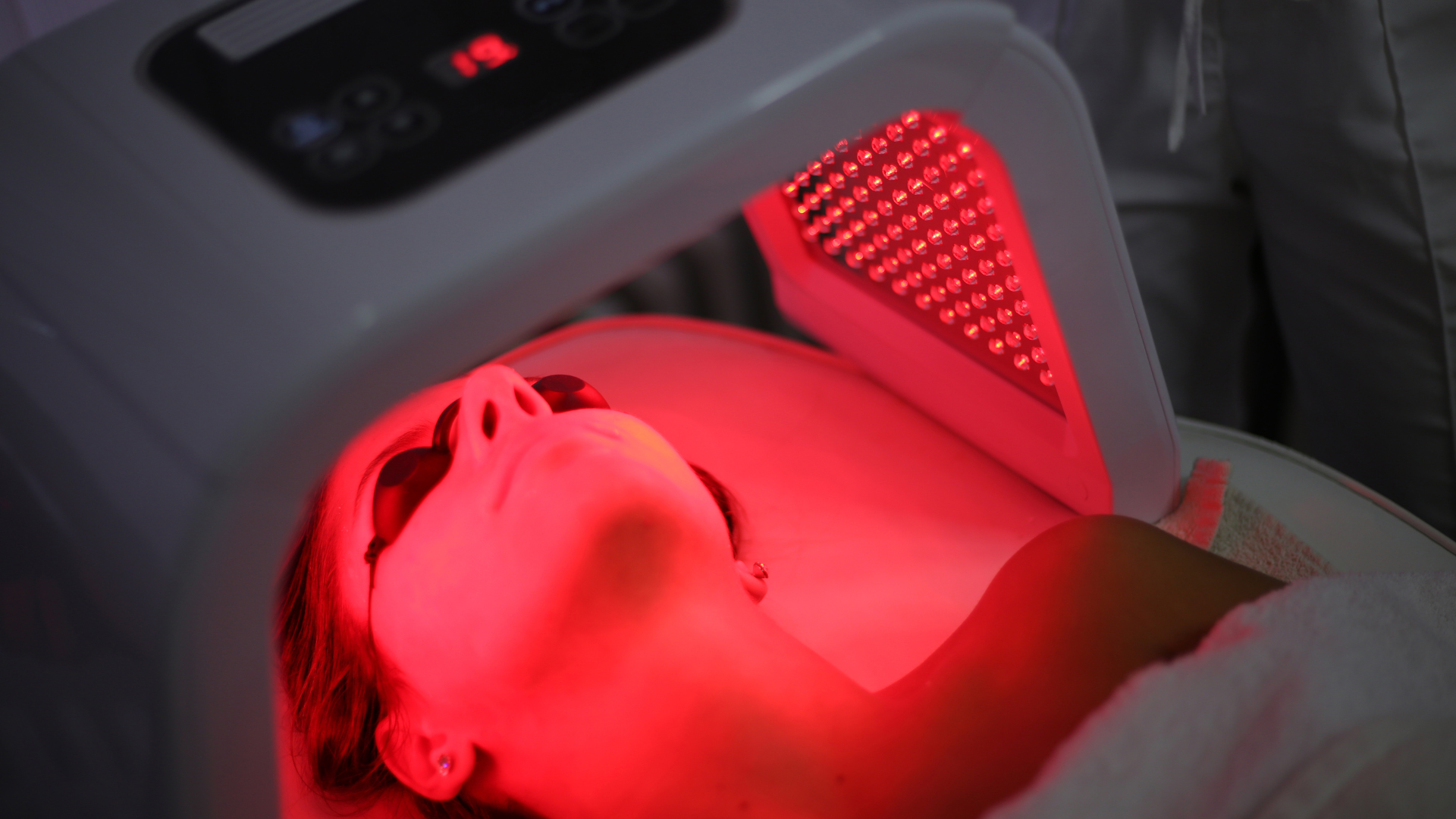 Person lying under a red LED light therapy device on a treatment bed