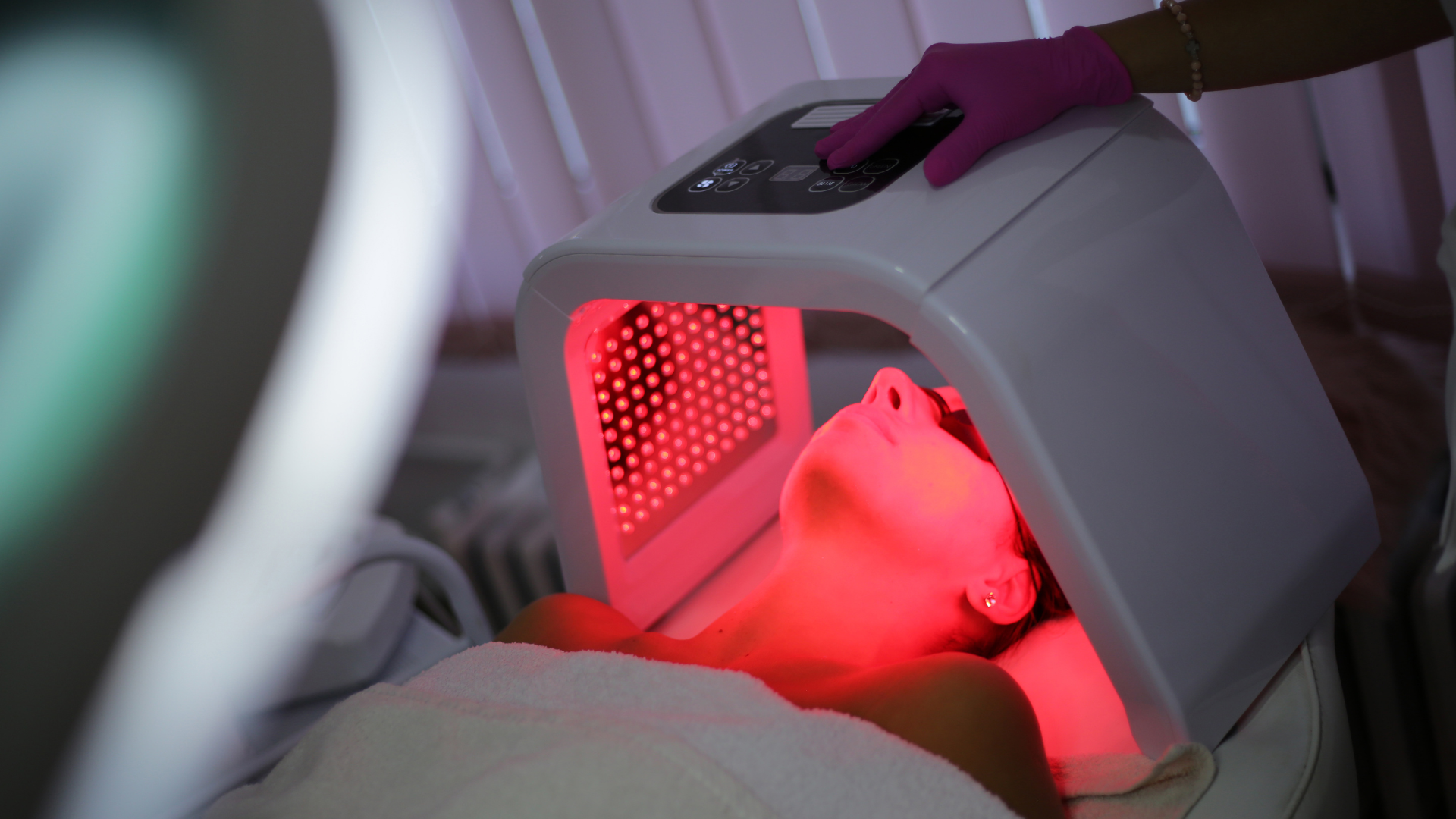 Person receiving red LED facial therapy under a white treatment hood