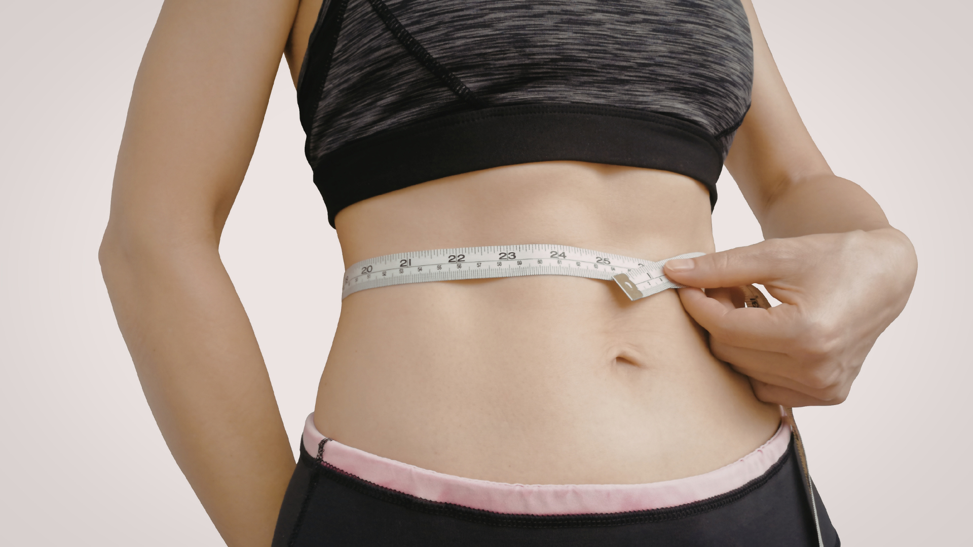 Person measuring waist with a tape measure against a bare midsection