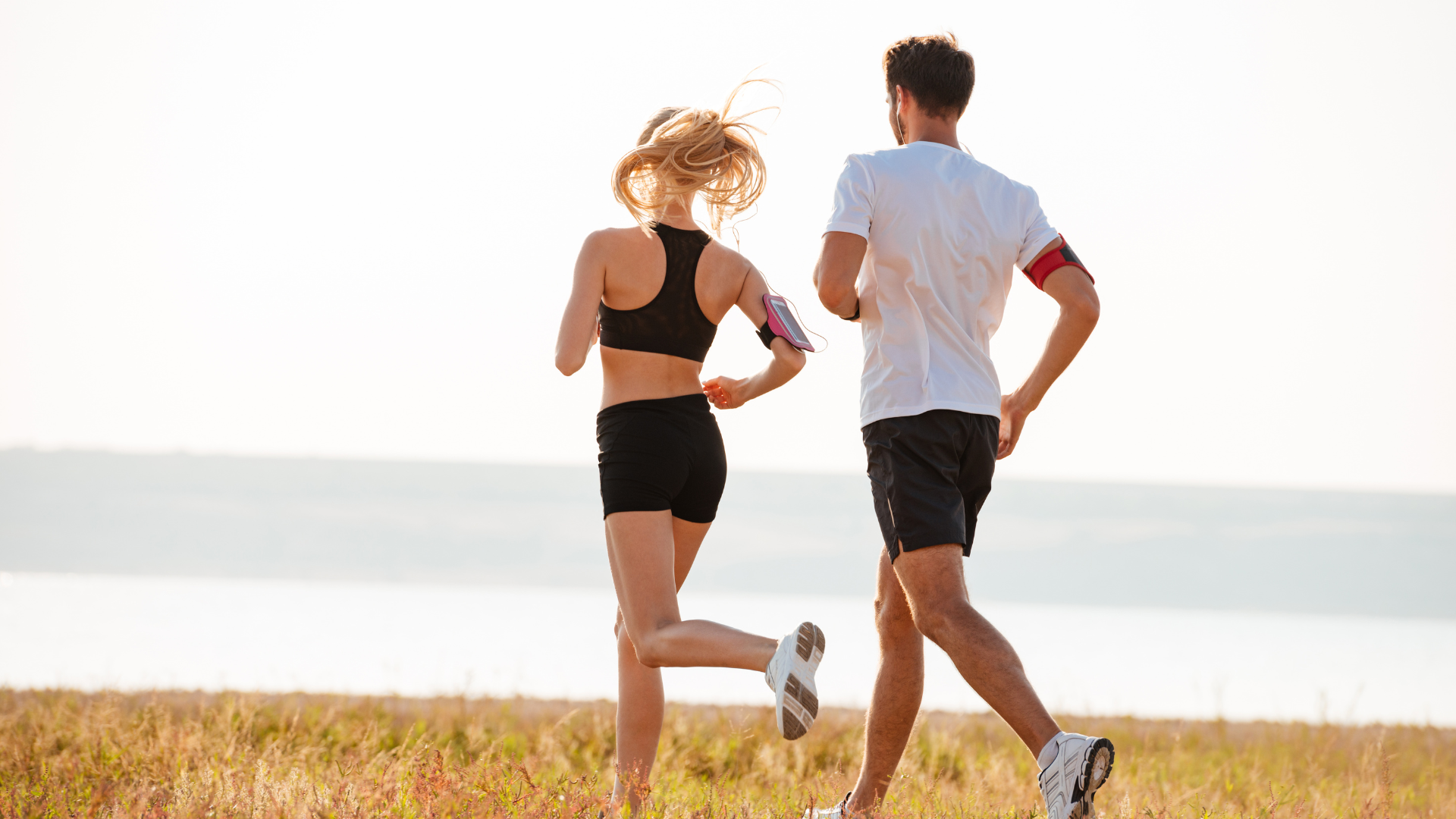 Two runners jogging by a shoreline, seen from behind, on a sunny day