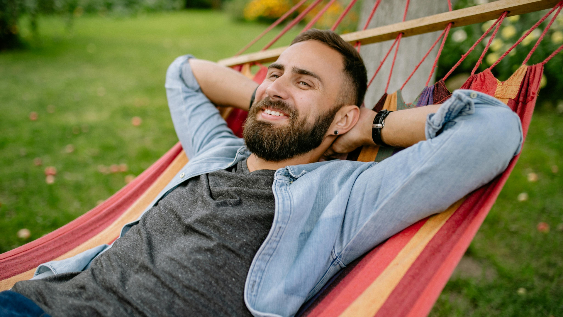 Man relaxing in a red hammock outdoors, hands behind head, smiling in a green park