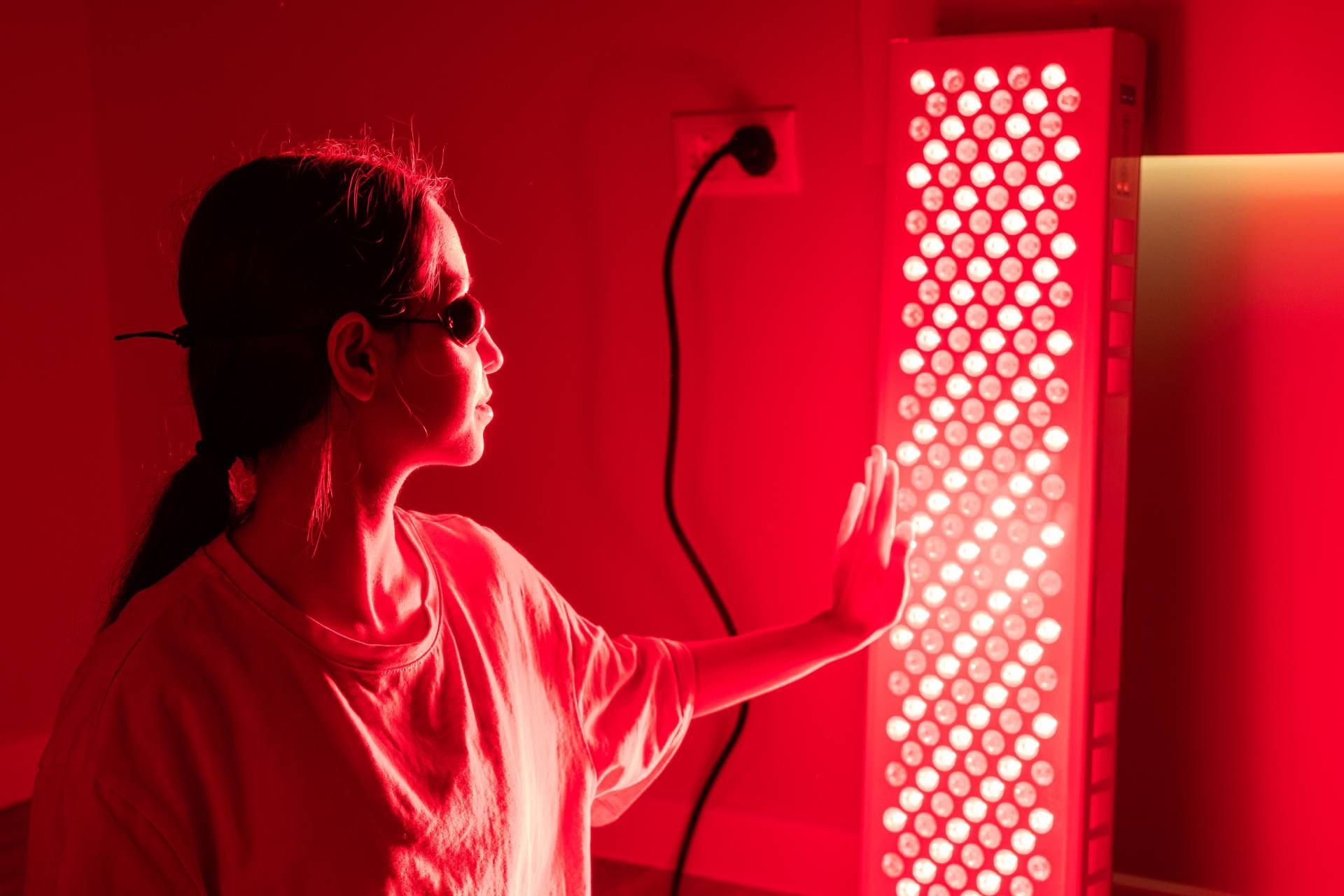 Person touching a glowing red light therapy panel in a dark room