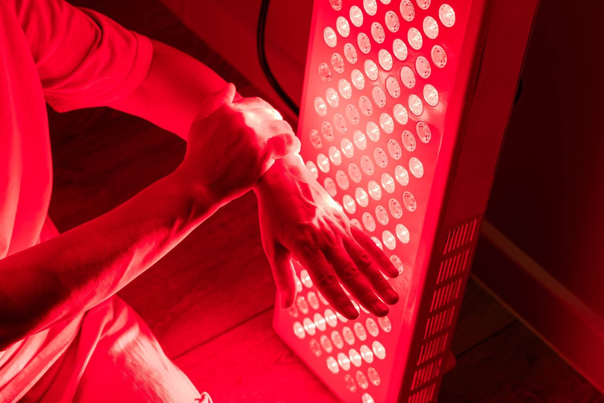 Person using a red LED therapy panel with both hands and forearms illuminated