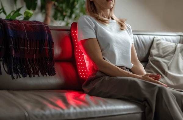 Person sitting on a gray couch with a red light panel behind them