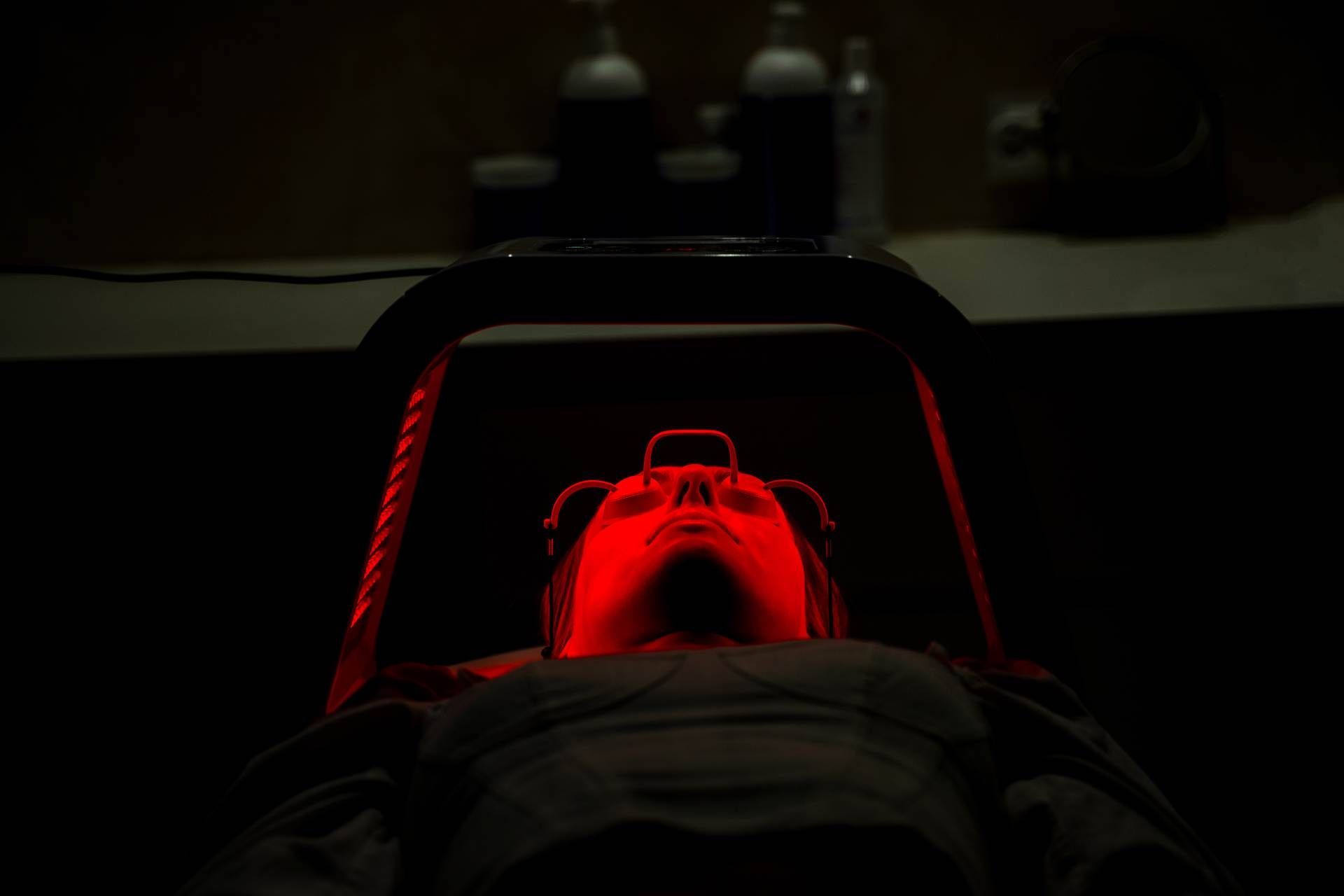 Person lying under a red medical light in a dark treatment room