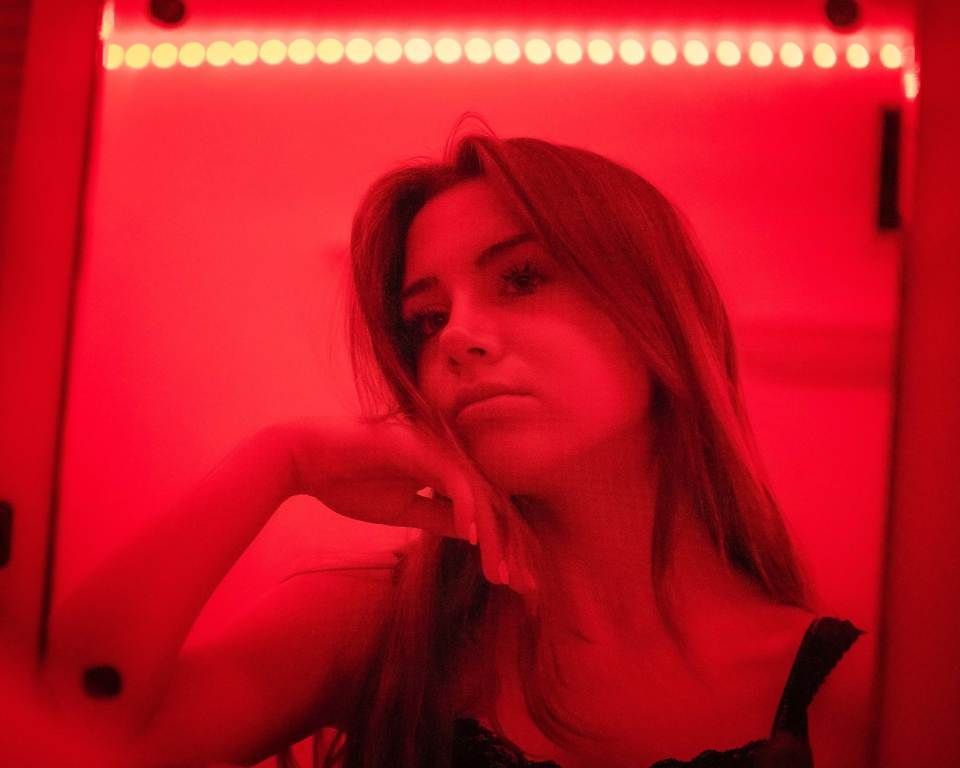 Woman posing under red neon light, resting her chin on her hand.
