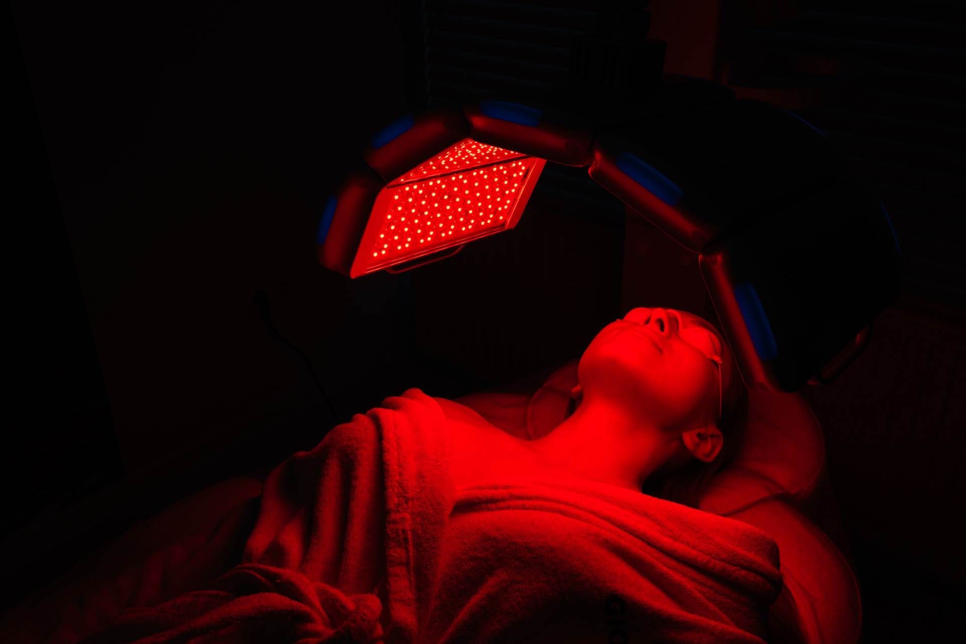 Person lying under a red light therapy panel in a dark room