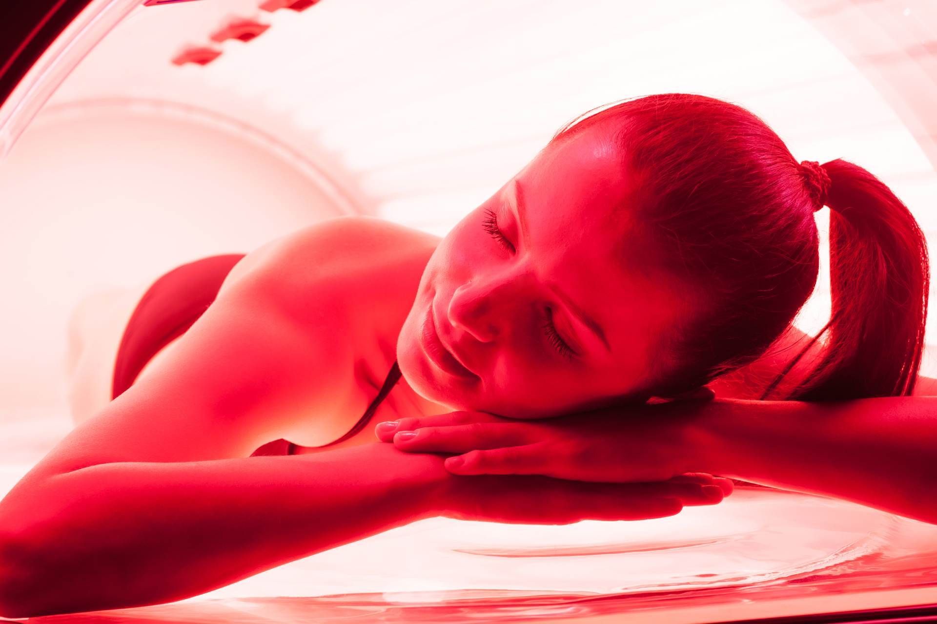 Person lying face down on a massage table under red lighting, resting their head on their hands.