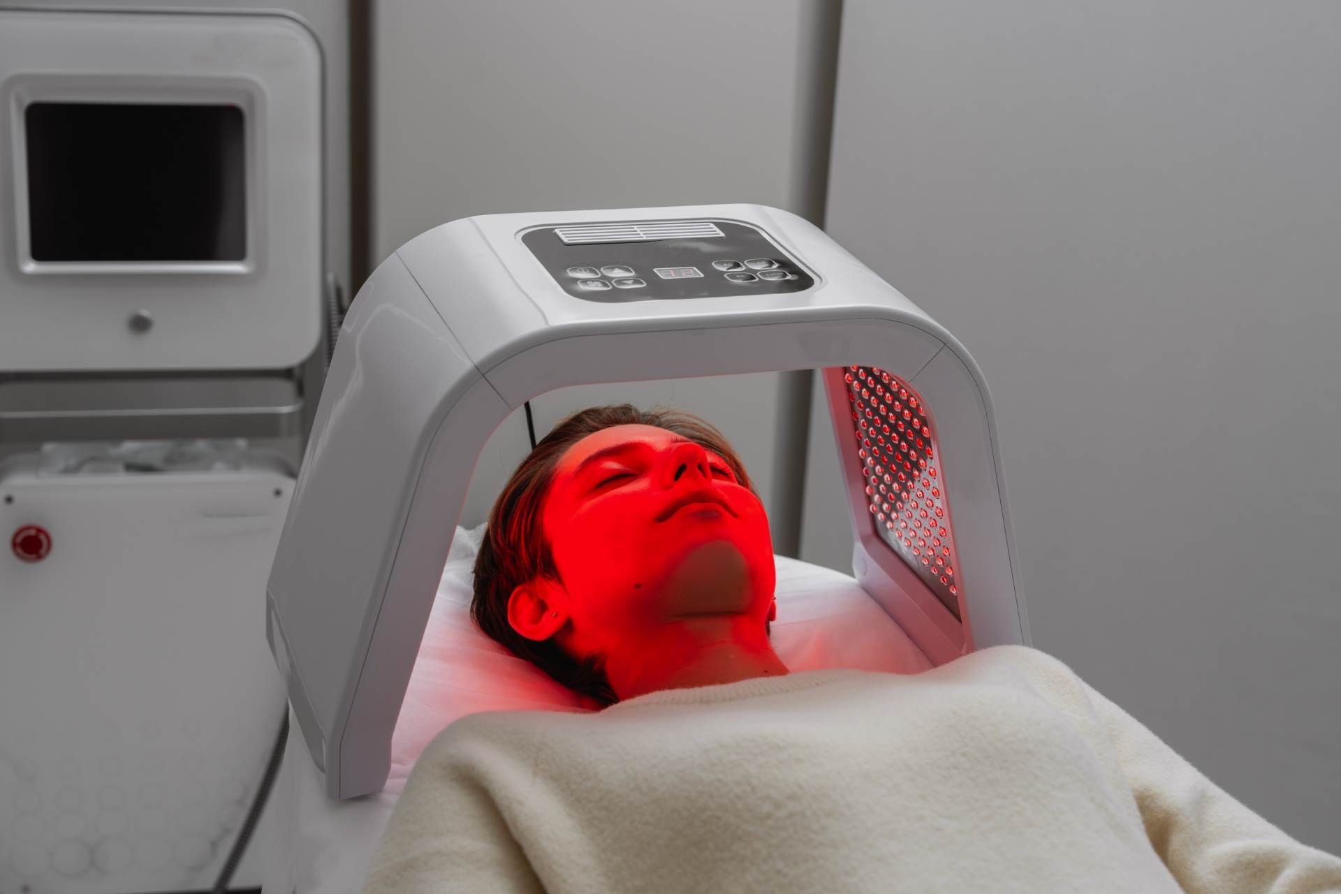 Person receiving red light therapy under a facial device in a clinical setting