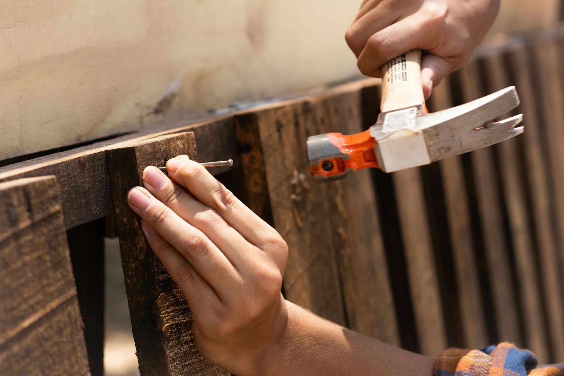 Person hammering a nail into wooden pallet.