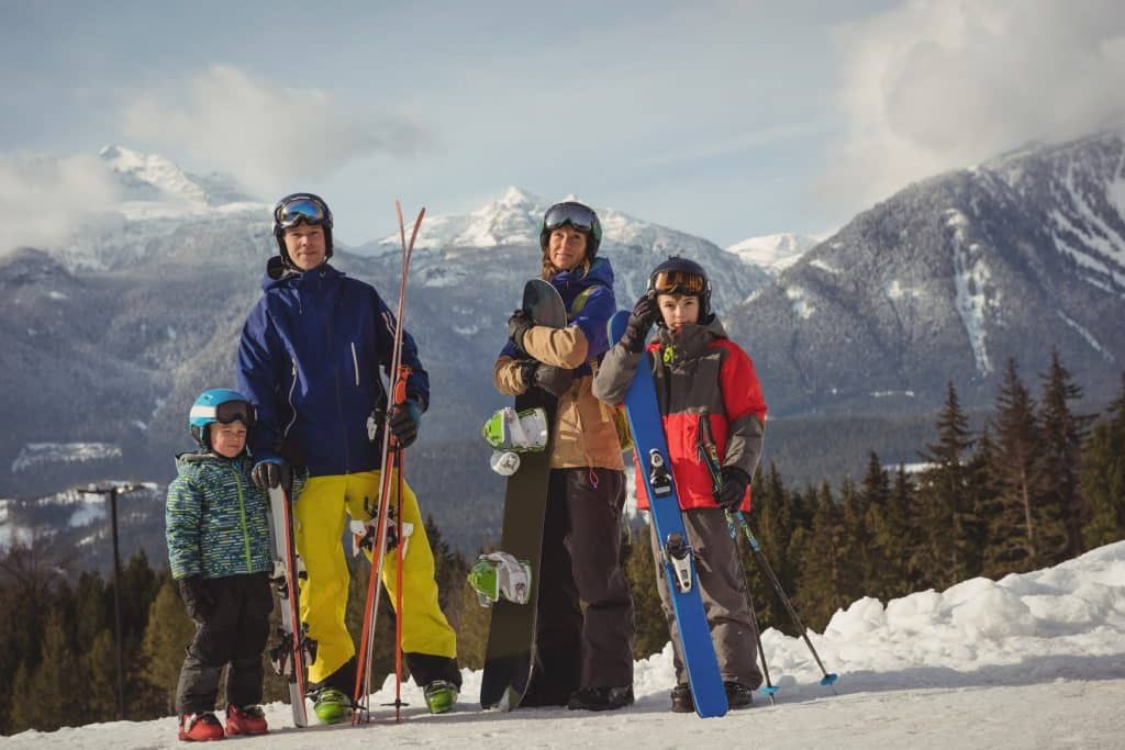 A family standing on top of a snow covered mountain with skis and snowboards.