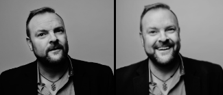 A man with a beard is smiling in a black and white photo.