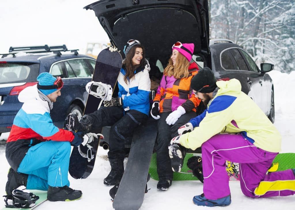 A group of snowboarders are sitting in the snow near a car.