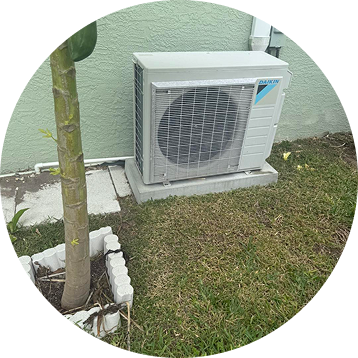 Air conditioning unit outside on a concrete base, next to a tree and a green wall.