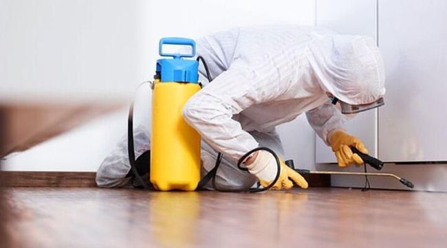 Un hombre con traje protector está rociando una habitación con un pulverizador.