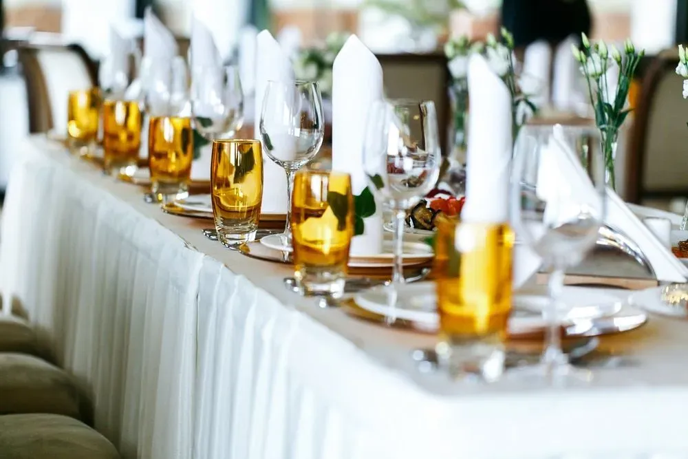A Long Table With Plates, Glasses, Napkins, and Flowers on it .