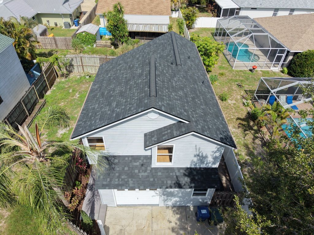 Aerial view of a gray house with a dark roof and white garage in a suburban yard.