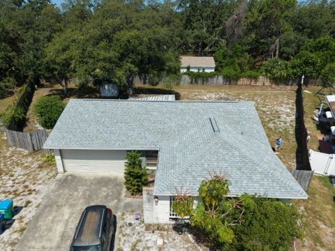 Aerial view of a gray-roofed house with a driveway, trees, and a parked car in a wooded area