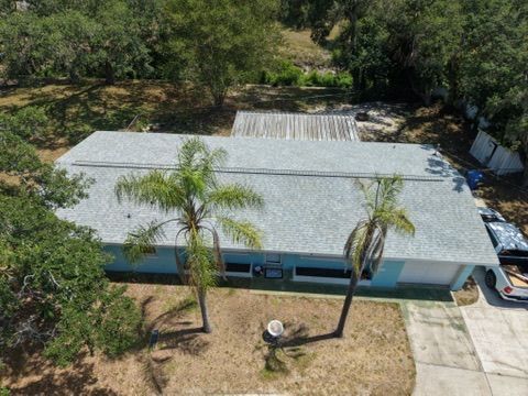 Aerial view of a single-story white house with palm trees and a driveway, surrounded by greenery.