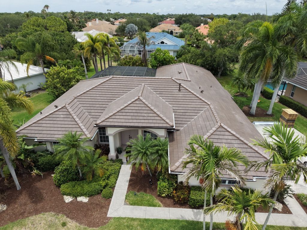 Aerial view of a large gray-roofed house surrounded by palm trees and lush tropical landscaping.