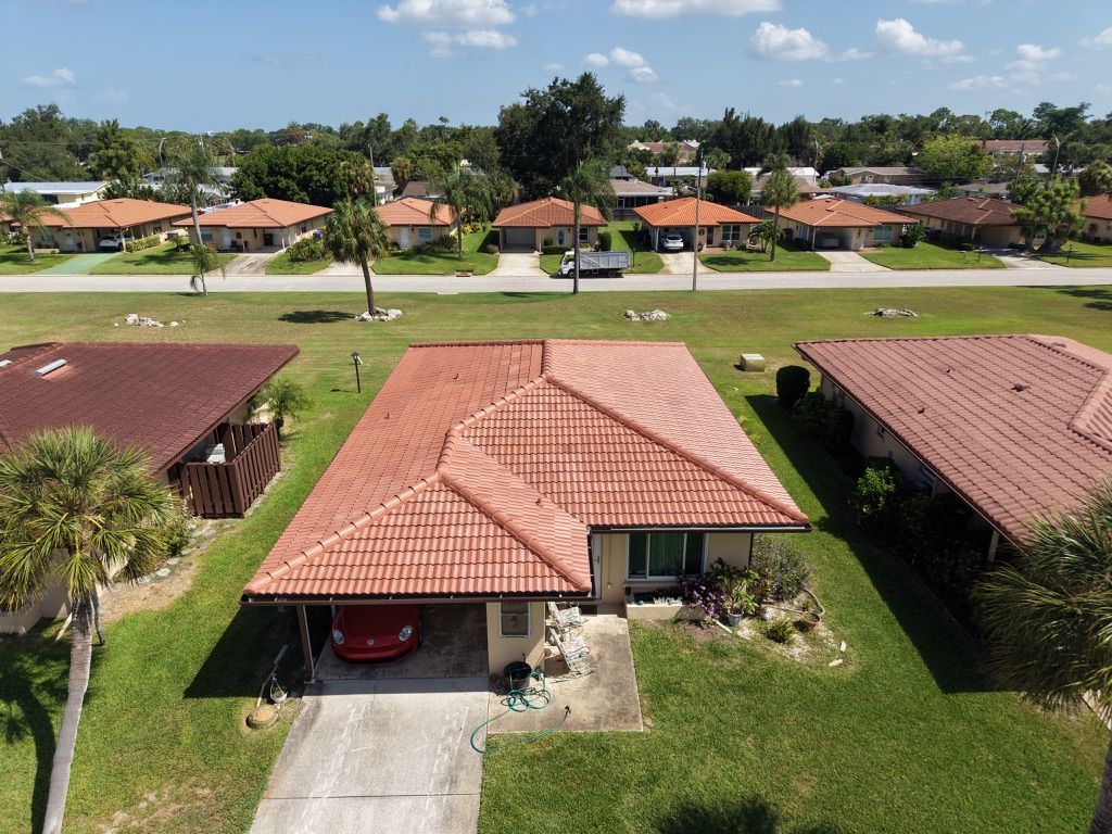 Aerial view of a beige house with a tiled roof, front palm trees, and a white SUV in the driveway.