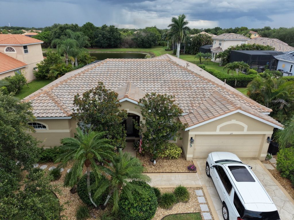 Aerial view of a beige house with a tiled roof, palm trees, and a white SUV parked in the driveway.