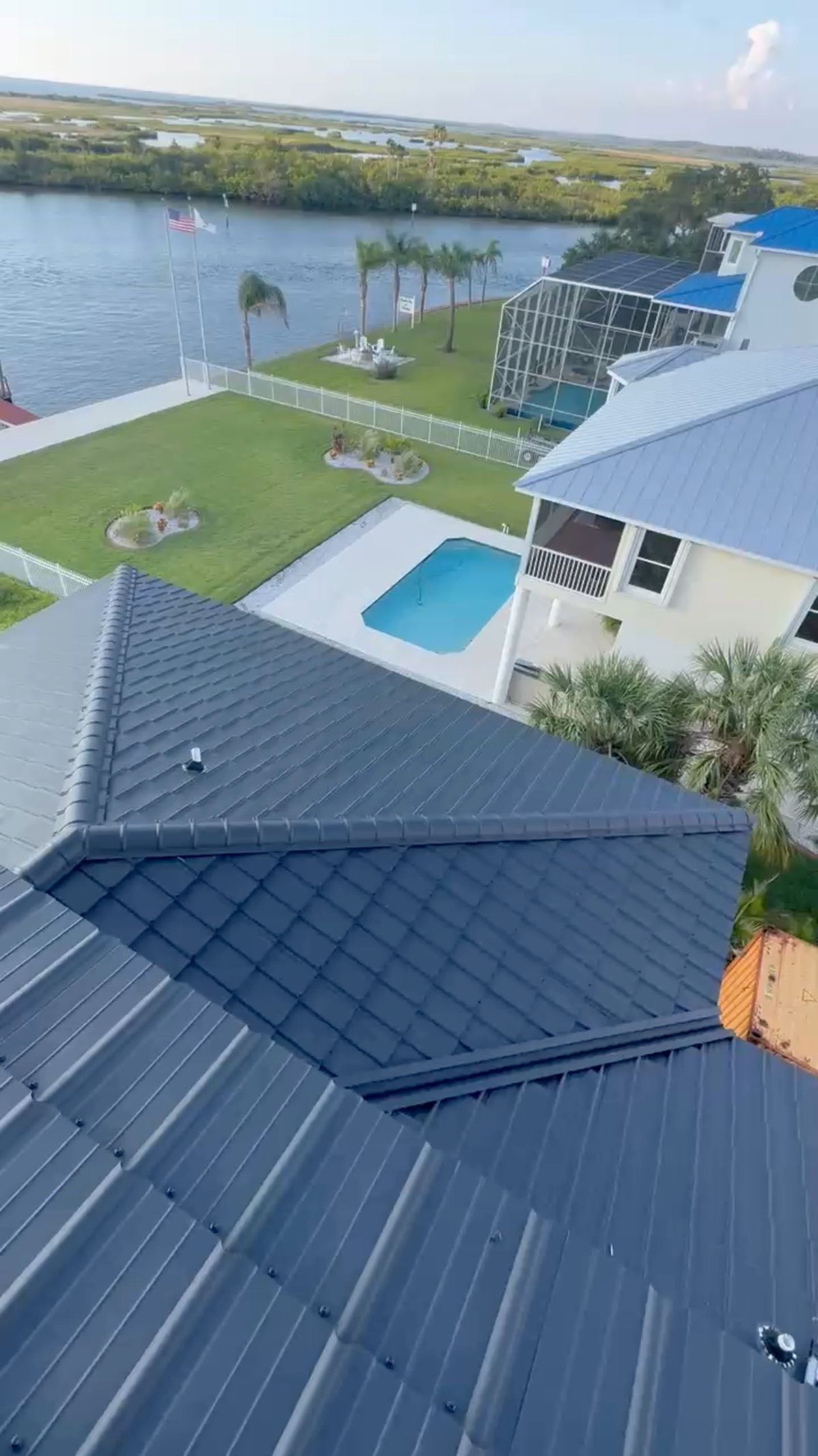 Aerial view of a light blue-roofed house with surrounding trees and yard.