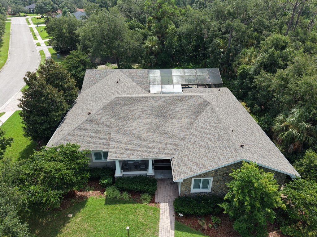 Aerial view of a house roof with workers on it, surrounded by trees and neighboring homes.