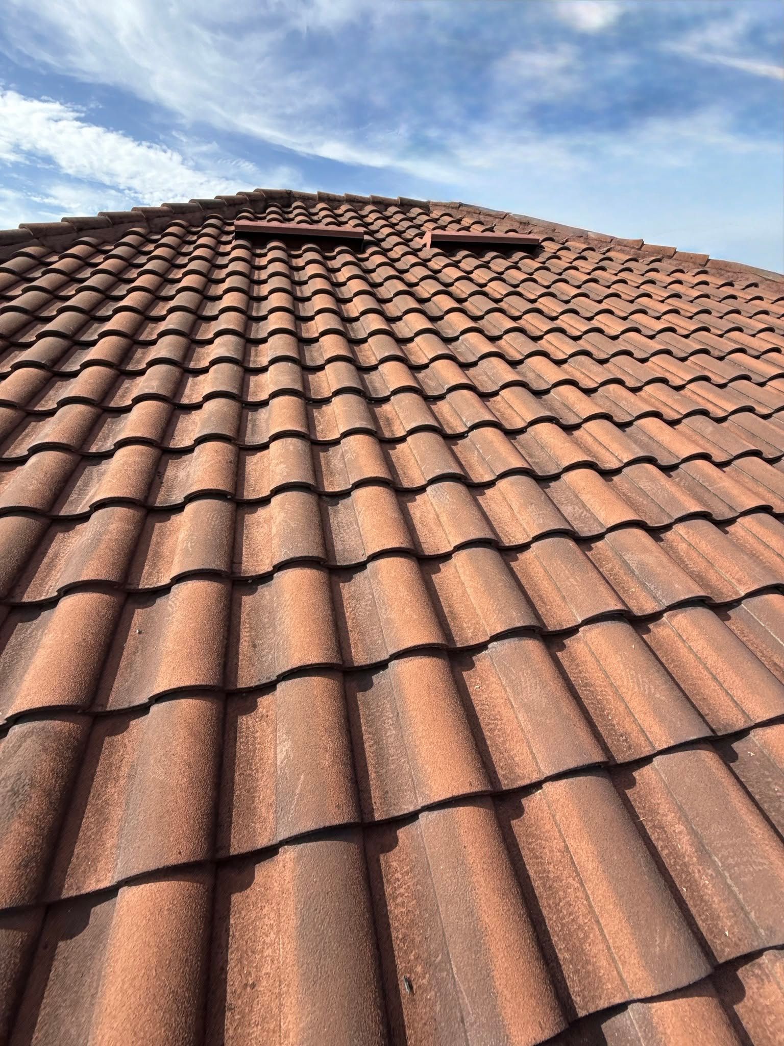 Red clay tile roof viewed from below against a blue sky with clouds