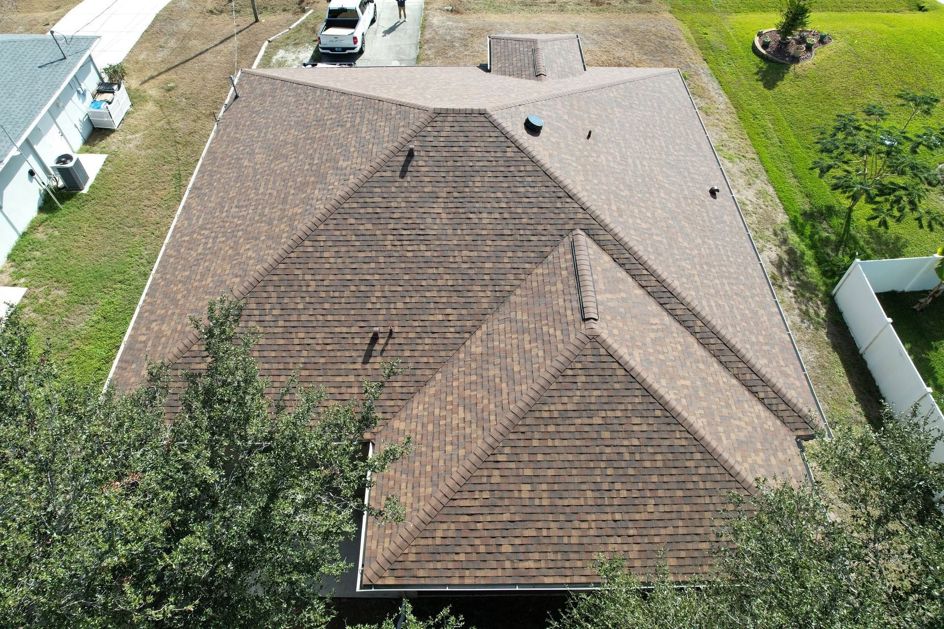 Aerial view of a brown shingle roof with trees and driveway around a suburban house