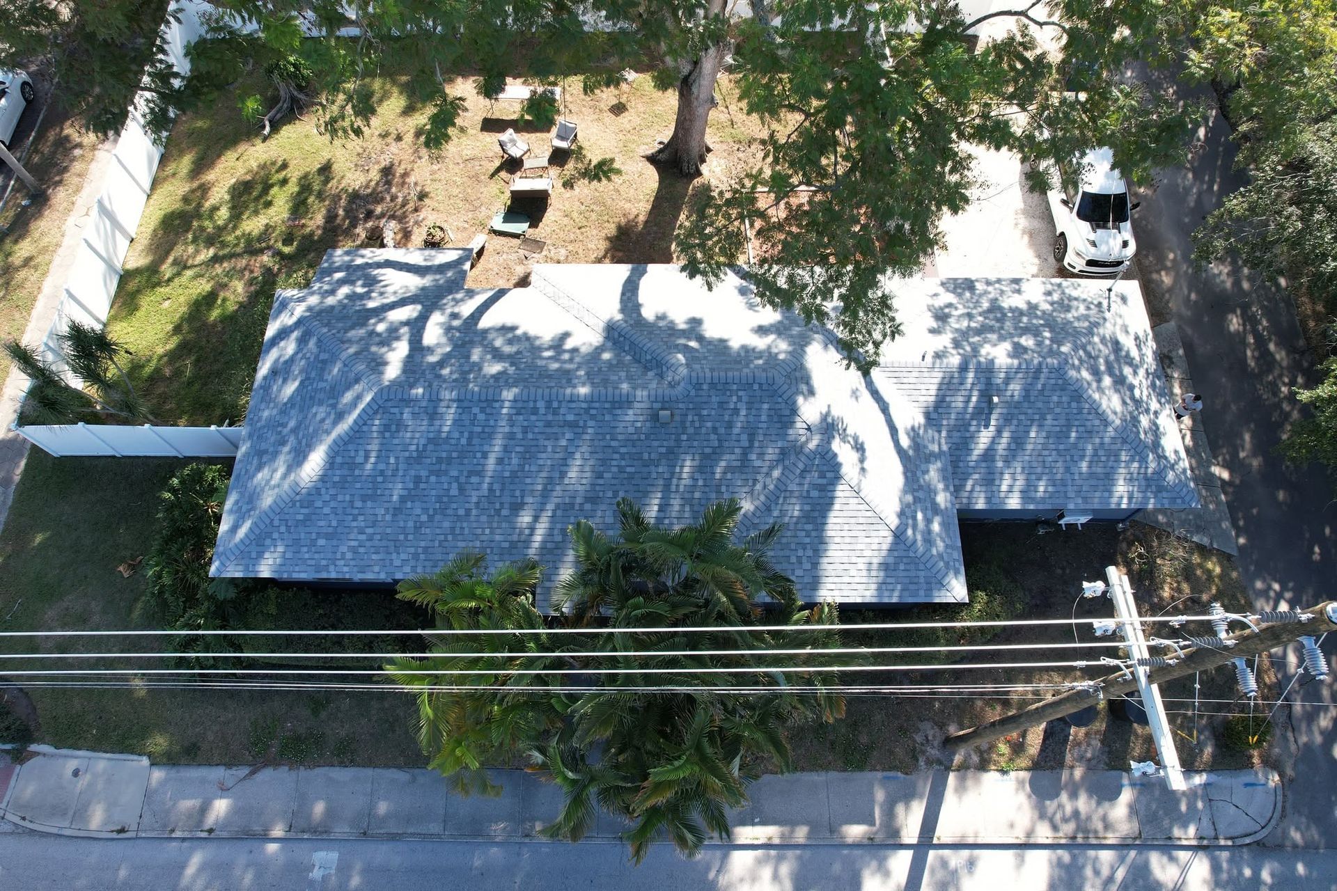 Aerial view of a house with a gray roof, trees, and utility lines along the street
