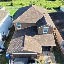 Worker cleaning moss off a shingled roof with a power washer, seen from above