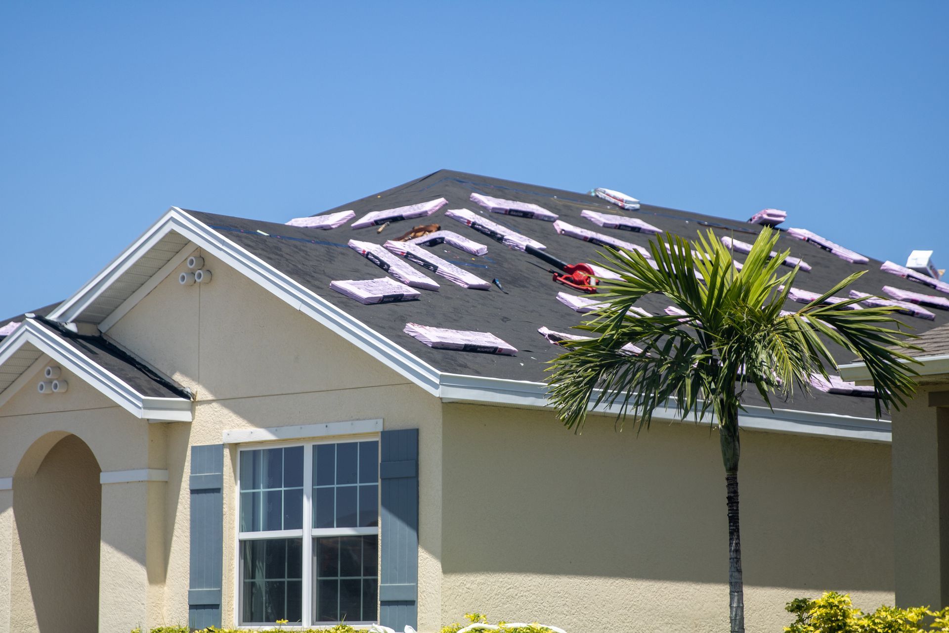 House roof with damage and scattered white debris near a palm tree on a sunny day