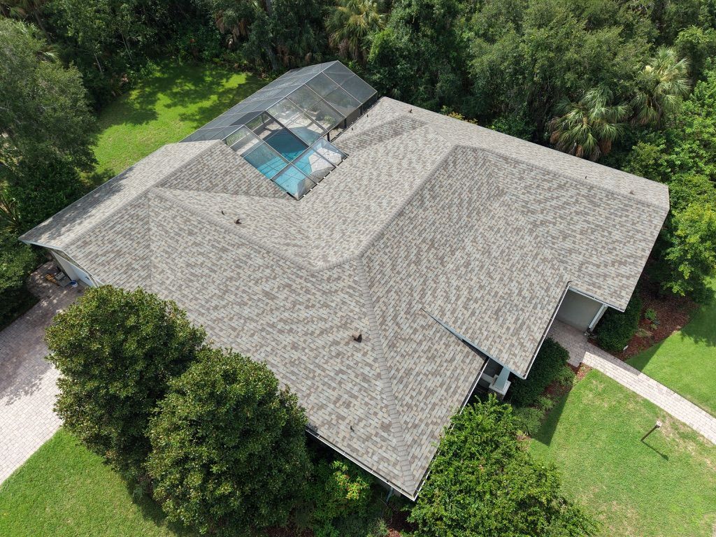 Roof peaks with dark gray shingles and light wood trim under green spring trees