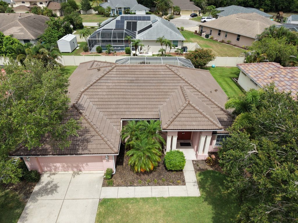 Aerial view of a brown shingled house roof with trees and a driveway nearby