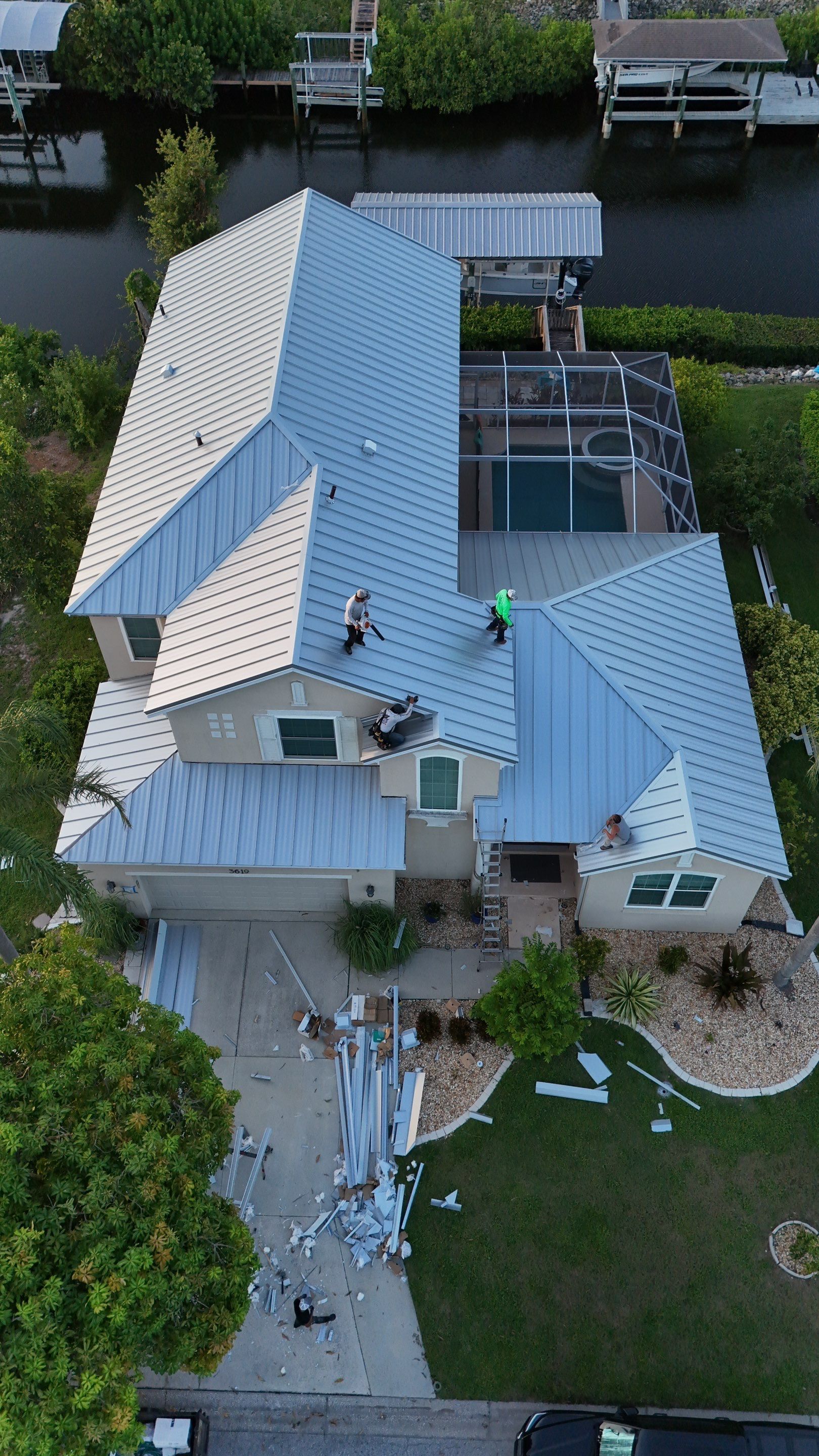 White metal roof on a house, viewed from above, with trees and parked vehicles in the background
