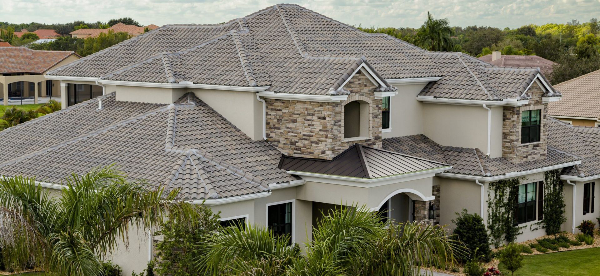 Two-story beige house with a gray shingle roof, white trim, and palm trees in front