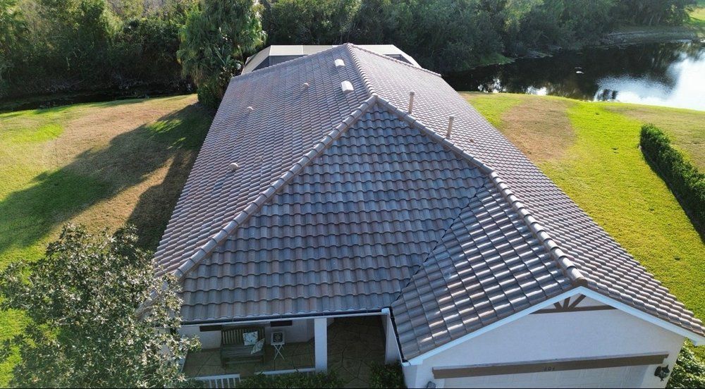 Aerial view of a house with a gray shingle roof beside trees and a pond.