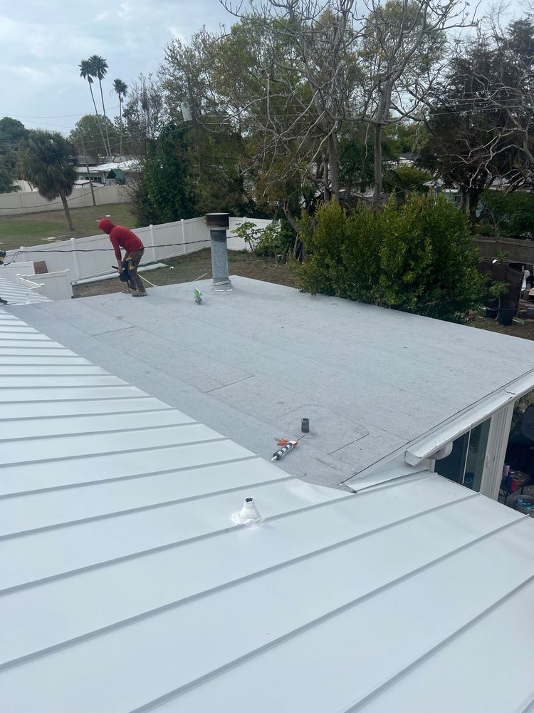 Worker on a flat rooftop near trees and shrubs, with light gray roofing sheets in the foreground.