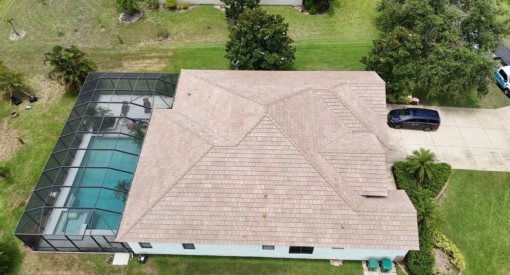 Aerial view of a house with a screened pool area, tan roof, green lawn, and a parked car in the driveway