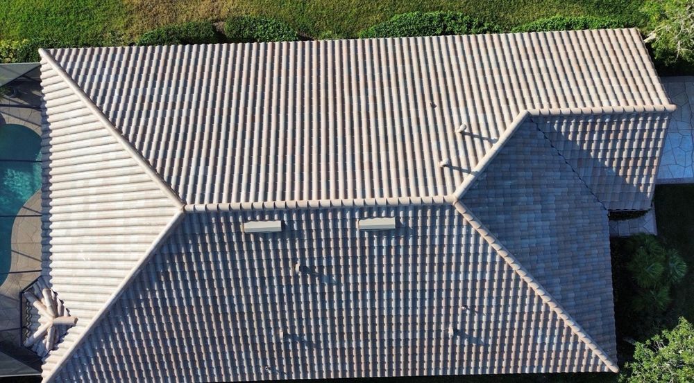 Aerial view of a house roof with gray tiles and two skylights, partly shaded by a tree