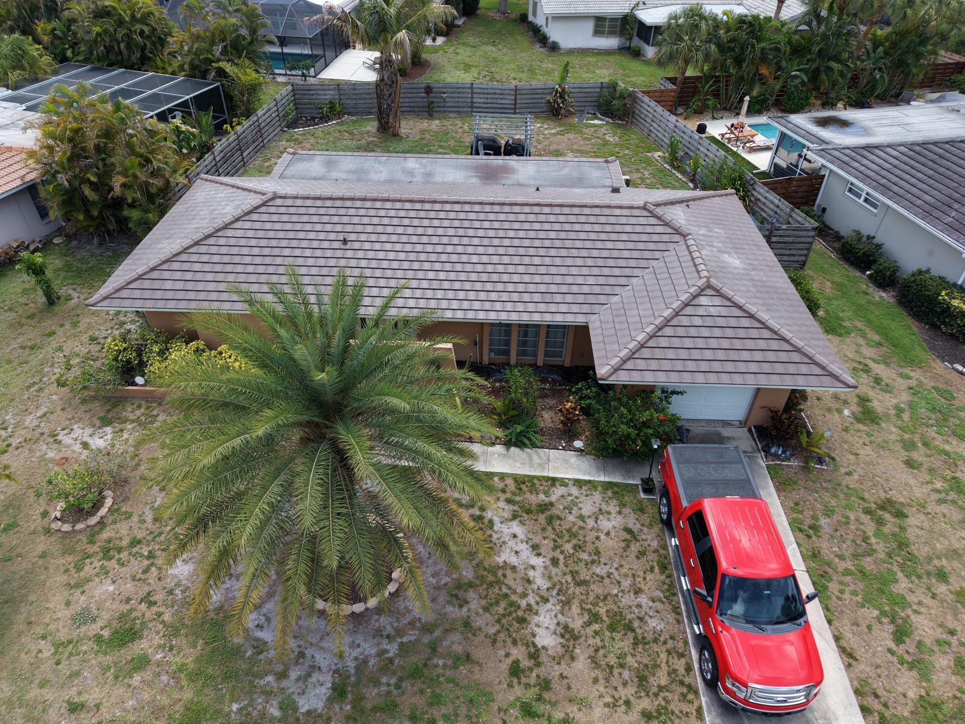Aerial view of a house with a gray roof, palm tree, and red car in the driveway.