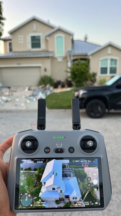 Hands holding a drone controller showing a live view of a suburban house and driveway on its screen