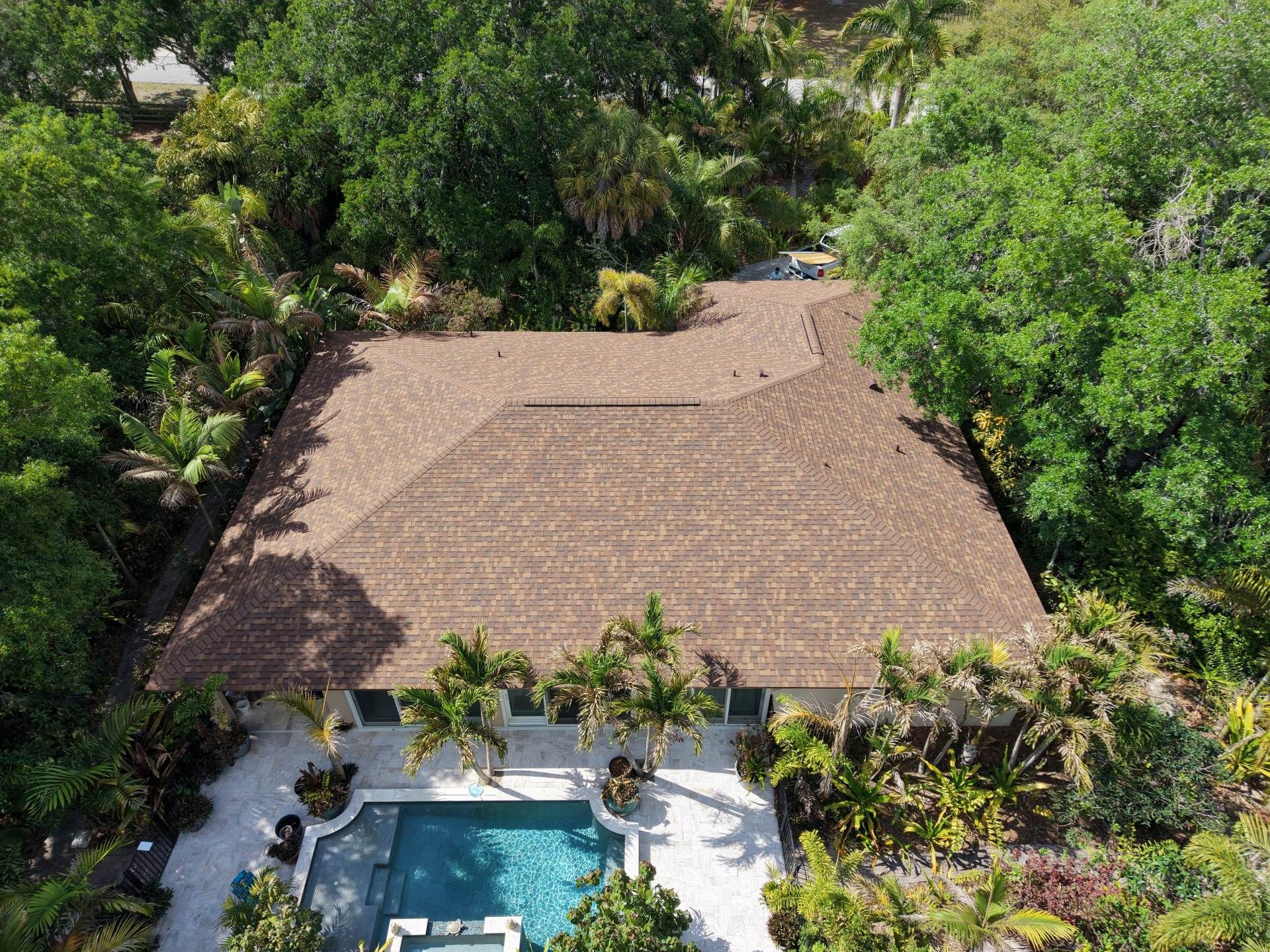 Aerial view of a tropical villa with a large thatched roof and swimming pool surrounded by lush trees
