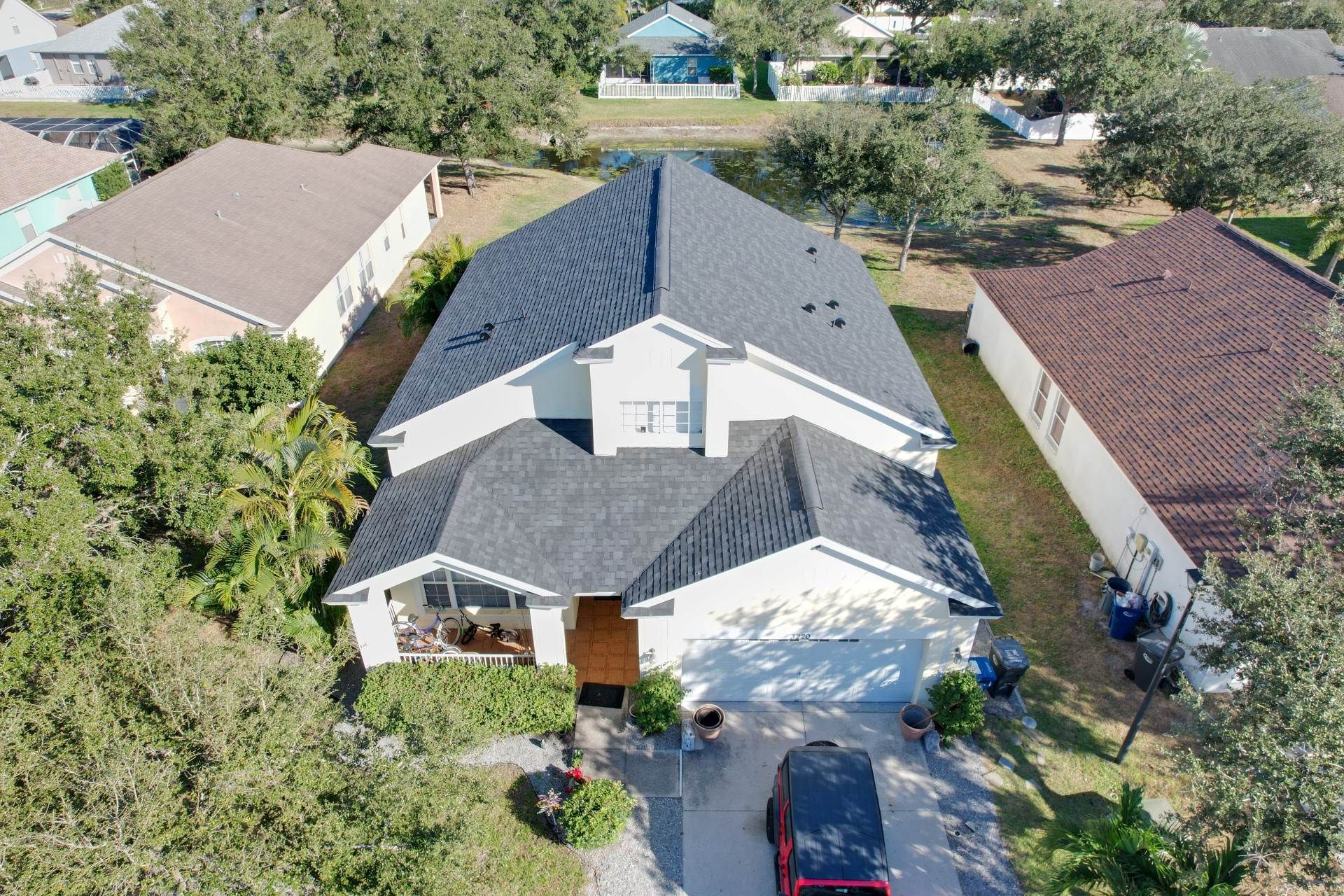 Aerial view of a suburban house with a gray roof, driveway, and surrounding trees.